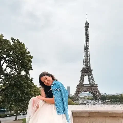 Camila de jaqueta jeans sentada num muro, com a Torre Eiffel atrás