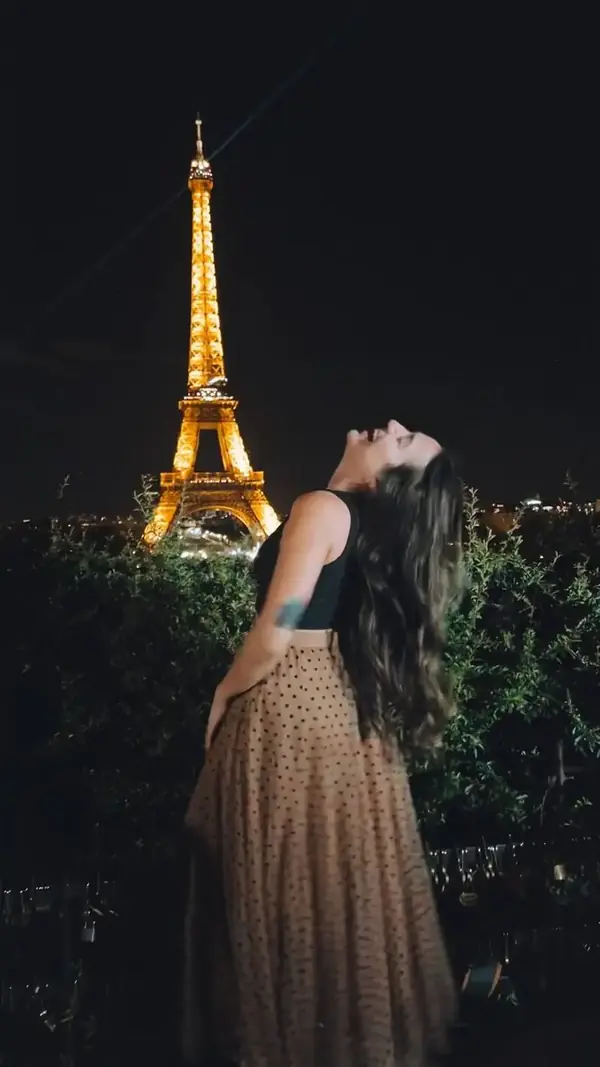 Camila olhando para cima, com a Torre Eiffel iluminada à noite