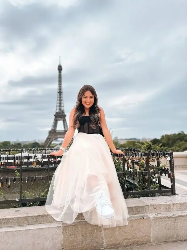 Camila sentada num muro, com a Torre Eiffel ao fundo