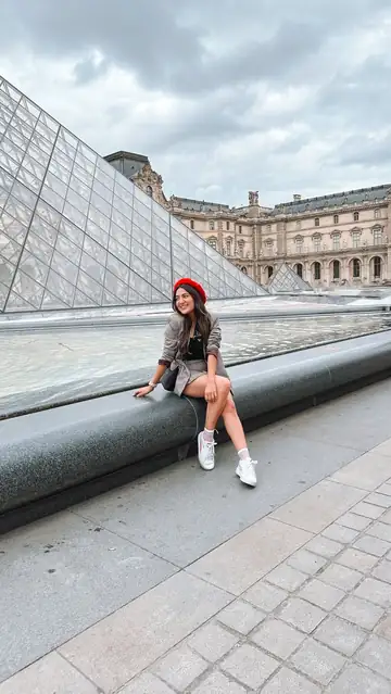 Camila sentada junto à pirâmide do Louvre