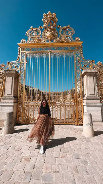 Camila diante do portão dourado do Palácio de Versalhes